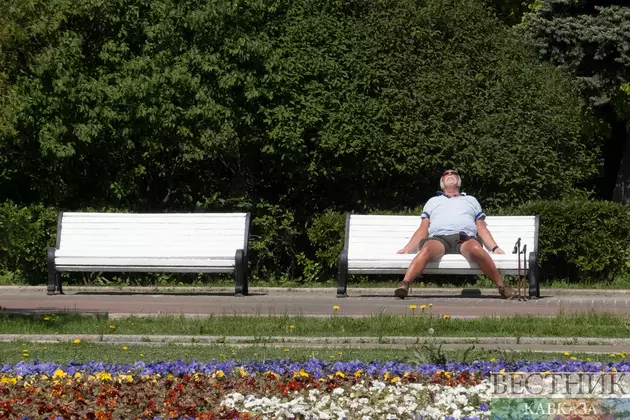 Мужчина загорает на скамейке в парке в жаркую погоду