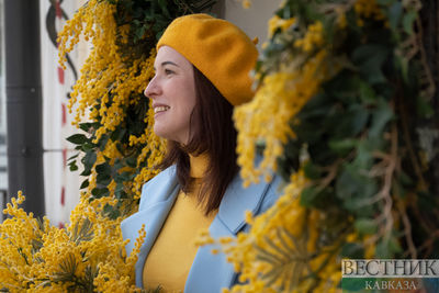 Девушка фотографируется на фоне украшенного мимозой магазина